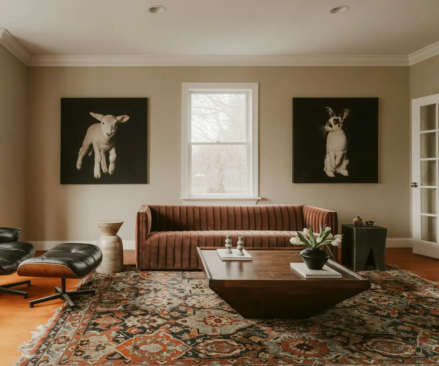 Salon avec canapé en velours brique, table basse en bois sombre, tapis persan et deux portraits d'animaux au mur.