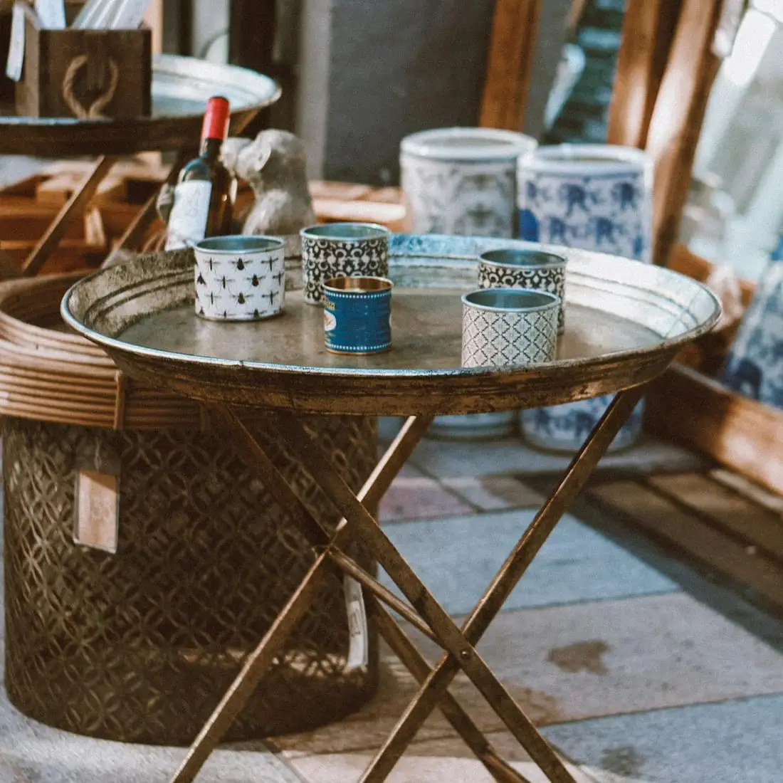 Table pliante en métal patiné, chargée de pots à motifs bleus et blancs, sur un trottoir de brocante.