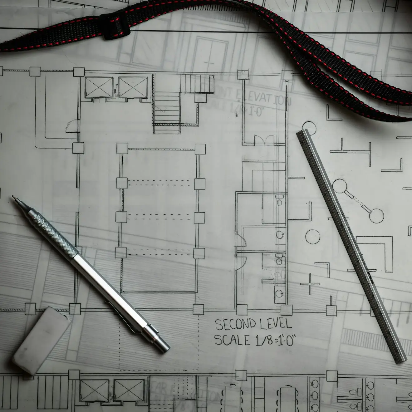Plan d'étage dessiné au crayon, avec un portemine, une règle et une gomme posés dessus.
